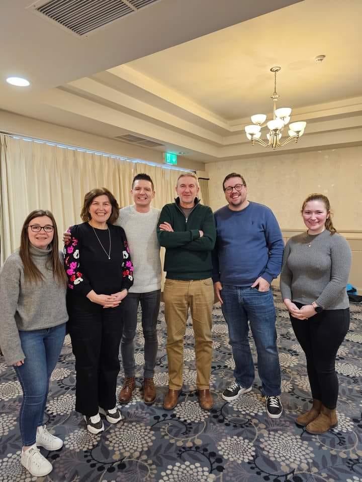 4 BBNI staff members standing in a row, at a conference for youth ministry, along with 2 of the event organisers