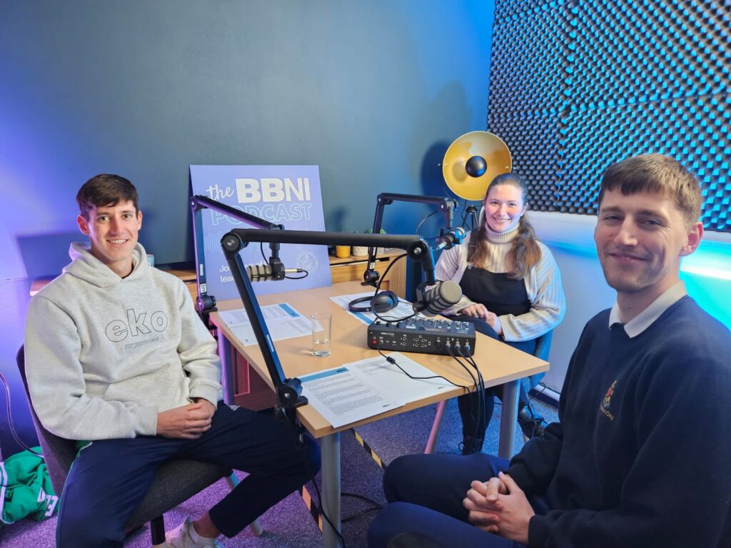 3 people sitting around a table recording a podcast for BBNI titled Playing Hockey and Being a Christian.